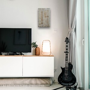 May include: A white wooden sign with a brown vintage guitar blueprint design. The sign is hanging on a white wall in a living room setting. A black electric guitar is on a stand in the foreground.