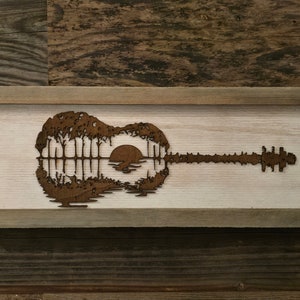 Puede incluir: Una pieza de arte de pared enmarcada en madera con una silueta de una guitarra con una puesta de sol y &aacute;rboles dentro del cuerpo de la guitarra.