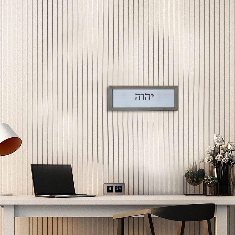 May include: A framed print with the Hebrew word "Chazak" in black lettering on a white background. The frame is silver and the print is hanging on a white wall.