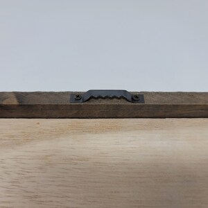 May include: Close-up of the back of a wooden framed sign with a black metal hanging hook attached to the top.