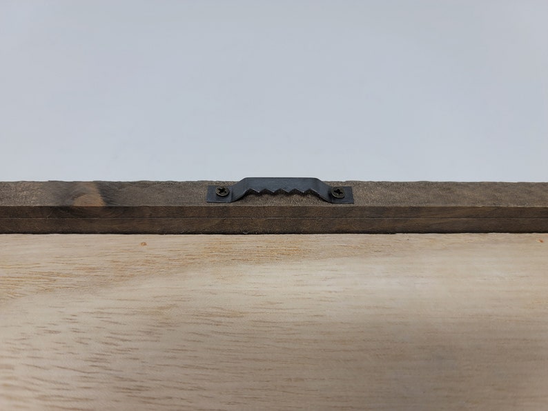 May include: Close-up of the back of a wooden framed sign with a black metal hanging hook attached to the top.