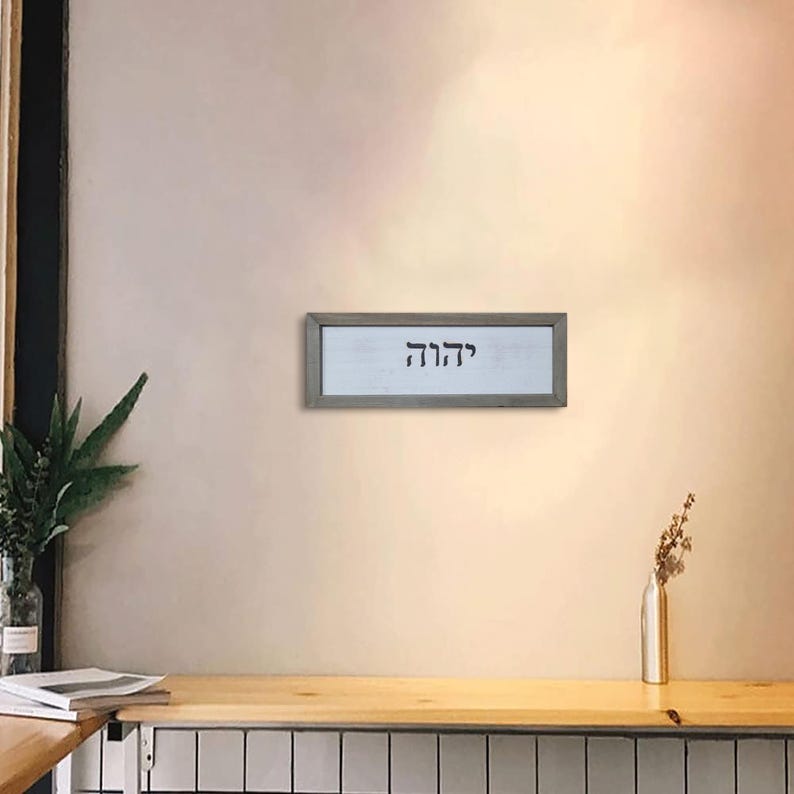 May include: A framed wall decor with the Hebrew word "Chai" written in black on a white background. The frame is a light gray wood.