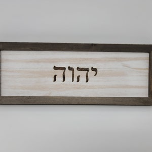 May include: A wooden sign with a dark brown frame and a white background. The Hebrew word "שלום" is carved into the wood.
