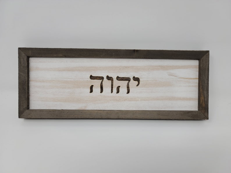 May include: A wooden sign with a dark brown frame and a white background. The Hebrew word "שלום" is carved into the wood.