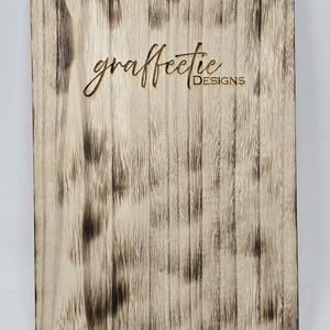 May include: A close-up of a wooden sign with the text "graffetie DESIGNS" burned into the surface. The wood has a distressed, weathered look.