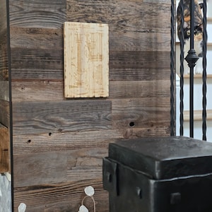 May include: A wood-panelled wall with a vintage guitar blueprint design printed on a wooden plaque. The plaque is mounted on the wall. A black metal stool is in the foreground.