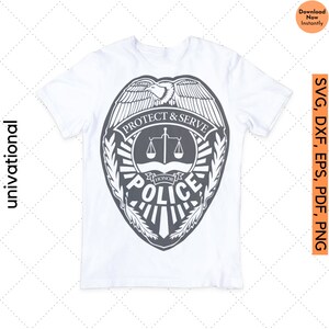 K&ouml;nnte beinhalten: Ein wei&szlig;es T-Shirt mit einem grauen Polizeibadge-Design. Das Abzeichen zeigt einen Adler, eine Waage und die Worte "Protect & Serve" und "Honor" mit dem Wort "Police" in einem Banner darunter.