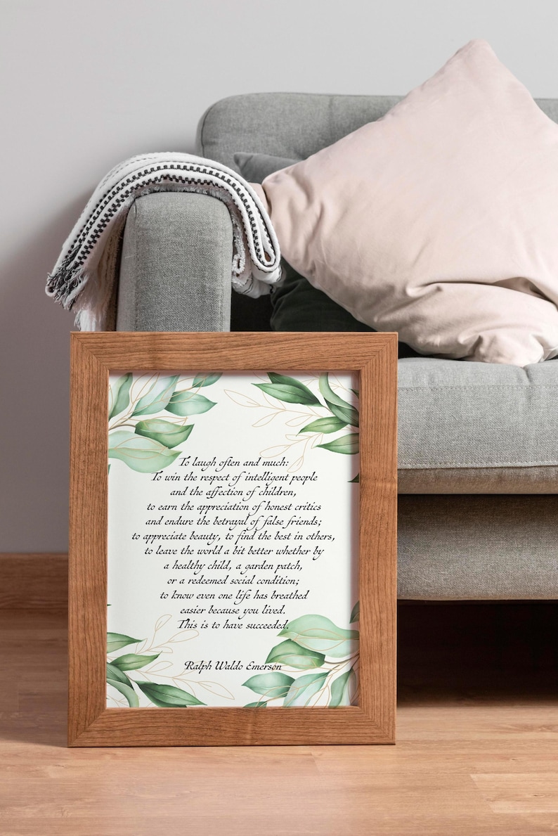 May include: A framed print with a wooden frame, featuring a quote by Ralph Waldo Emerson. The quote is in black text on a white background, with green botanical accents. The frame is brown and the print is displayed on a gray couch.