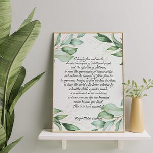 May include: A framed print with a gold border featuring a quote by Ralph Waldo Emerson, surrounded by watercolor green leaves. The print is displayed on a white shelf with a small yellow vase and greenery.