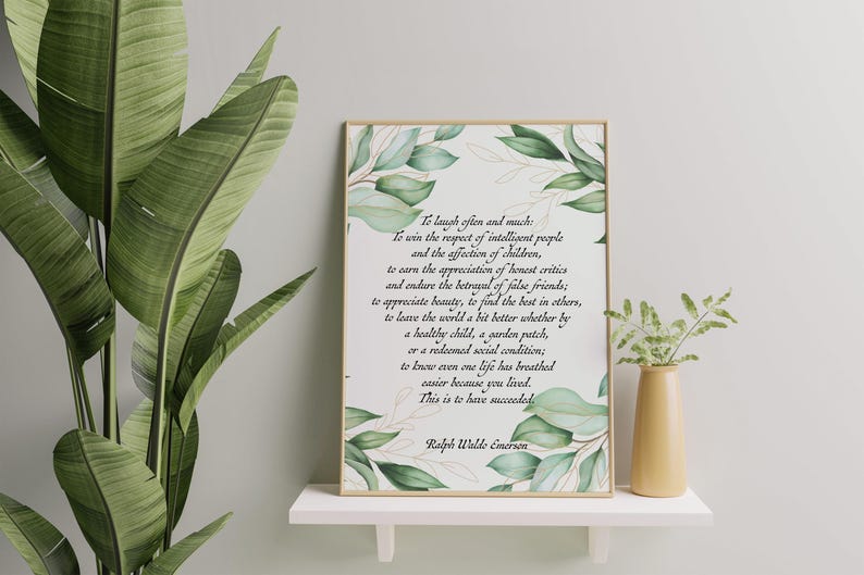May include: A framed print with a gold border featuring a quote by Ralph Waldo Emerson, surrounded by watercolor green leaves. The print is displayed on a white shelf with a small yellow vase and greenery.