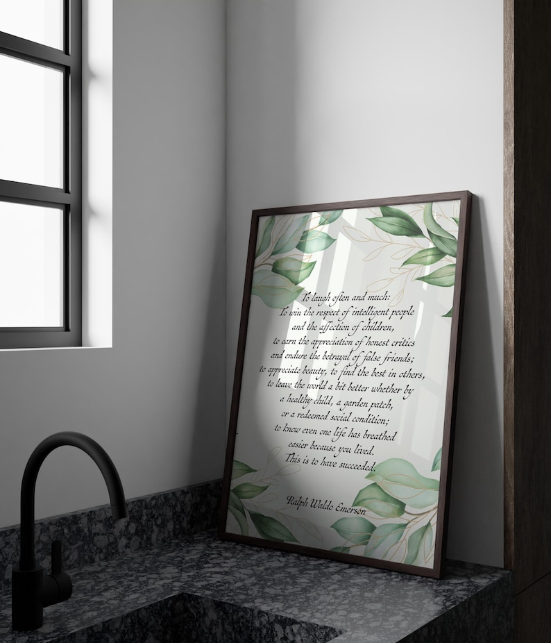 May include: A framed print with a brown border, featuring a quote by Ralph Waldo Emerson. The text is in a script font, with green leaf and gold accents. The print is leaning against a wall next to a window and a black faucet.