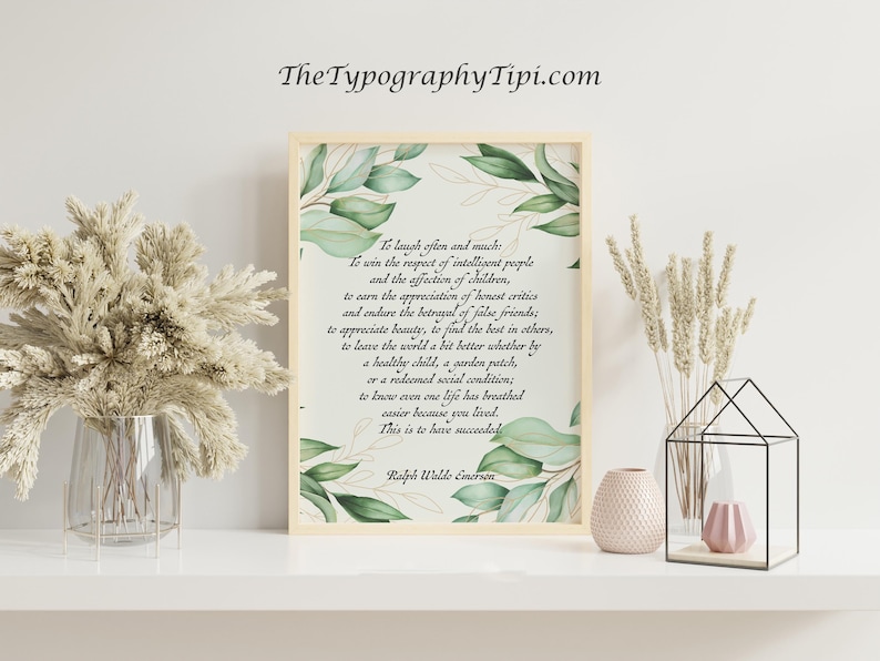 May include: A framed print with a quote by Ralph Waldo Emerson, surrounded by green watercolor leaves. The print is displayed on a white shelf with decorative vases and dried plants. The text reads "To laugh often and much..."