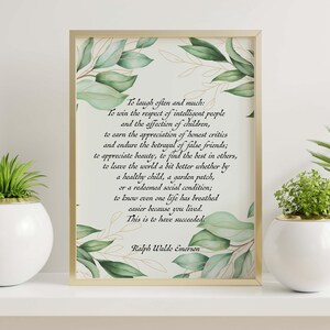 May include: A framed print with a gold border featuring a quote by Ralph Waldo Emerson, surrounded by watercolor-style green leaves. Two white spherical planters with green plants are on either side.