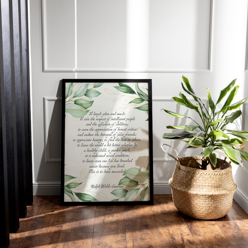 May include: A framed print with a black border features a quote by Ralph Waldo Emerson, surrounded by green and gold leaf illustrations. A woven basket with a green plant sits to the right of the print, adding a natural element to the scene.