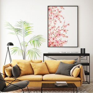 Puede incluir: Una pintura de acuarela de una rama de flor de cerezo rosa sobre un fondo blanco. La pintura est&aacute; enmarcada en un marco negro y colgada en una pared blanca sobre un sof&aacute; amarillo.