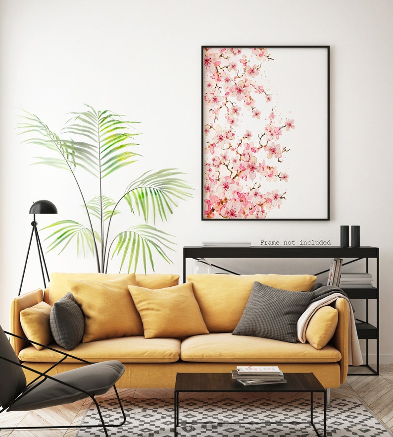 Puede incluir: Una pintura de acuarela de una rama de flor de cerezo rosa sobre un fondo blanco. La pintura est&aacute; enmarcada en un marco negro y colgada en una pared blanca sobre un sof&aacute; amarillo.
