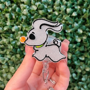 May include: A white glitter  retratable badge holder with a cartoon image of Zero, the ghost dog from the movie The Nightmare Before Christmas. Zero is wearing a green collar and has a glowing orange nose.
