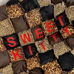 May include: A brown, black, and leopard print patchwork quilt with the word "SWEET KITTY" sewn in red letters.