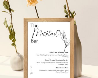 May include: A framed sign with the text "The Mocktail Bar" in black cursive font. The sign lists three mocktail recipes: Kiwi-Lime Sparkling Mint, Blood Orange Rosemary Spritz, and Strawberry Pom.