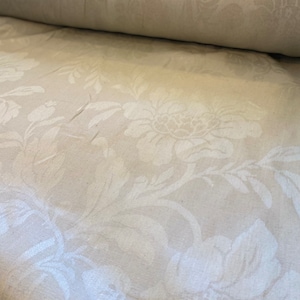 May include: White fabric with a raised floral pattern. The fabric is rolled up and the pattern is visible on both the top and bottom of the roll.
