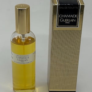 Könnte beinhalten: Eine klare Glasflasche Chamade Guerlain Eau de Toilette mit goldenem Verschluss und gelber Flüssigkeit, begleitet von der hohen rechteckigen Schachtel. Die Schachtel zeigt goldene und schwarze geometrische Muster mit dem Text Chamade Guerlain Paris 93 ml.