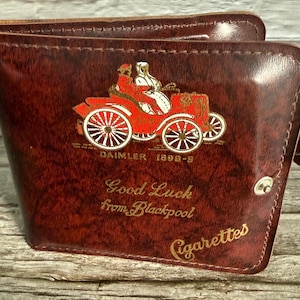 Op de afbeelding: Bruin leren portemonnee met een rode en gouden illustratie van een klassieke auto. De portemonnee heeft de tekst "DAIMLER 1898-9", "Good Luck from Blackpool" en "Cigarettes" in gouden letters.