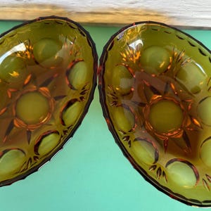 Könnte beinhalten: Zwei ovale Servierschalen aus bernsteinfarbenem Glas. Jede Schale hat ein Sternmuster in der Mitte und dekorative Ränder. Das Glas hat eine glänzende Oberfläche und reflektiert das Licht. Vintage.