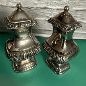 Puede incluir: Una taza de cerámica blanca con un asa negra y el texto "But First, Coffee" en negrita negra. La taza está sobre una superficie de madera. La taza mide aproximadamente 10 cm de alto.