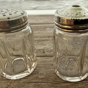 Peut inclure: Deux salières et poivrières vintage en verre avec des couvercles en métal argenté. Les salières en verre transparent ont un design à facettes. L'une a un dessus perforé, l'autre un seul trou.