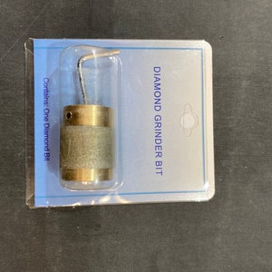 Peut inclure: Un embout de meuleuse diamantée emballé dans un contenant en plastique transparent. L'embout a une surface de meulage cylindrique et texturée et une base en métal couleur laiton. L'emballage est bleu clair avec le texte "DIAMOND GRINDER BIT".