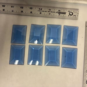 May include: Eight rectangular, light blue glass pieces with a beveled edge are arranged in two rows. A ruler with inch measurements is in the background. The glass pieces are approximately 1.5 inches by 1 inch.