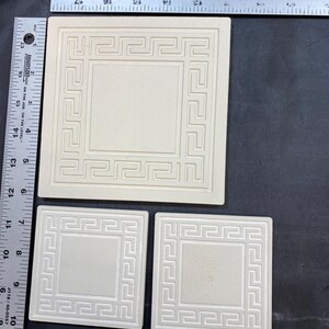 May include: Three ceramic tiles with a white background and a raised, embossed, white Greek key border design.
