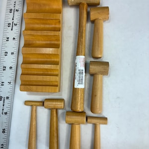 May include: A collection of wooden mallets and a curved wooden form. The mallets vary in size, with cylindrical and rectangular heads. The wood has a light brown color. A ruler is in the background.