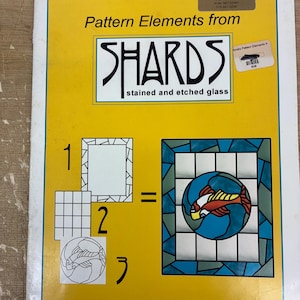 Peut inclure: Un livre intitulé "Pattern Elements from SHARDS stained and etched glass" avec une couverture jaune. La couverture présente des schémas de motifs de vitraux, dont un motif de poisson dans une fenêtre en vitrail bleu et vert.