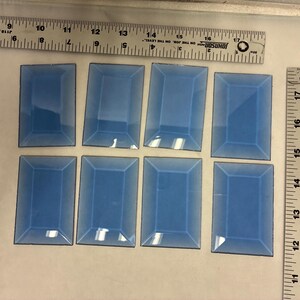 May include: Eight rectangular, light blue glass tiles with black borders are arranged on a white surface. Two rulers are positioned above and to the right of the tiles, providing measurement references in inches.