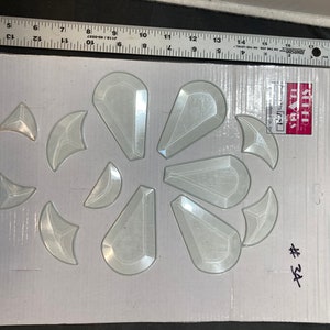 May include: A sheet of clear plastic with 12 different shapes of glass pieces. The shapes are all geometric and include triangles, crescents, and teardrop shapes. The sheet is labeled "Stained Glass" and "#34".