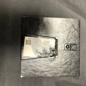 May include: Black leather picture frame with a white label that says "PBS" and a silver clasp.