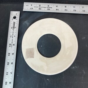 May include: A white ceramic ring with a hole in the center. The ring is approximately 4 inches in diameter.