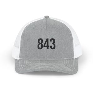May include: A gray trucker hat with a white mesh back and a curved brim. The number "843" is printed in bold black font on the front of the hat. The hat has a classic, casual style.