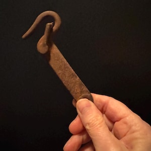 May include: A rusty metal hook with a curved handle. The hook is held in a hand.