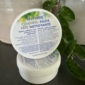 May include: A white plastic jar of Norwex Cleaning Paste with a blue label. The label reads "Cleans, polishes and protects in one application." and "Nettoie, polit et protège en un seule opération." The jar is 6.76 fluid ounces or 200 milliliters.
