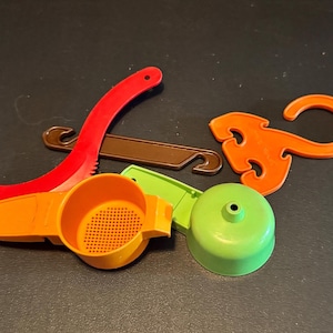 May include: A collection of colorful plastic kitchen tools, including a red curved tool, a brown hook-shaped piece, an orange juicer, a green lid, and an orange decorative hook. These items are likely for food preparation.