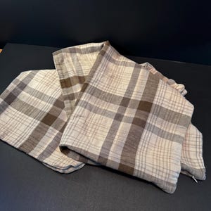 May include: A pair of square throw pillow covers featuring a plaid pattern in shades of cream, beige, and dark brown. The fabric has a visible woven texture, and each cover includes a small, discreet zipper closure along the bottom edge.