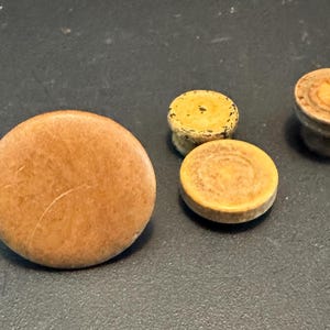 May include: A collection of four small, wooden objects in varying shapes and sizes. The objects are primarily shades of brown and tan, with a large, flat, round piece and several smaller, circular pieces, one with a pedestal base.