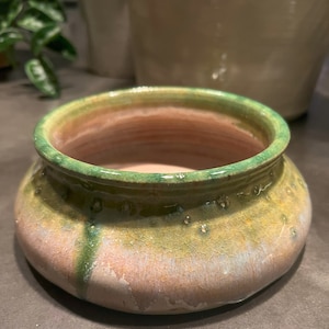 May include: A small, round ceramic planter with a green rim and a speckled glaze in shades of green, brown, and white.