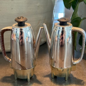 May include: Two silver metal salt and pepper shakers shaped like vintage coffee pots. The shakers have black plastic lids and gold accents.