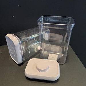 May include: Clear, rectangular food storage containers with white lids. One container is upright, another is on its side, and a lid is separate. The containers are made of clear plastic and have a square shape.