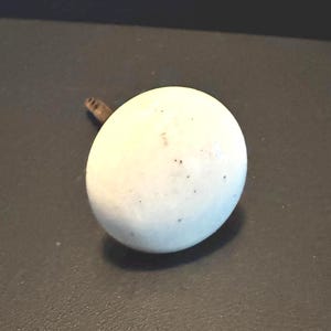 May include: A white, egg-shaped knob with a small, dark brown stem. The knob has a slightly speckled surface and is set against a dark background. This decorative hardware is suitable for cabinets and drawers.