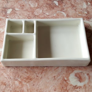 May include: White ceramic tray with four compartments. The tray has a rectangular shape with a raised edge and a smooth surface.