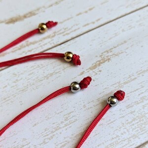 May include: Three red cords with gold and silver beads at the ends. The cords are knotted at the ends with the beads.